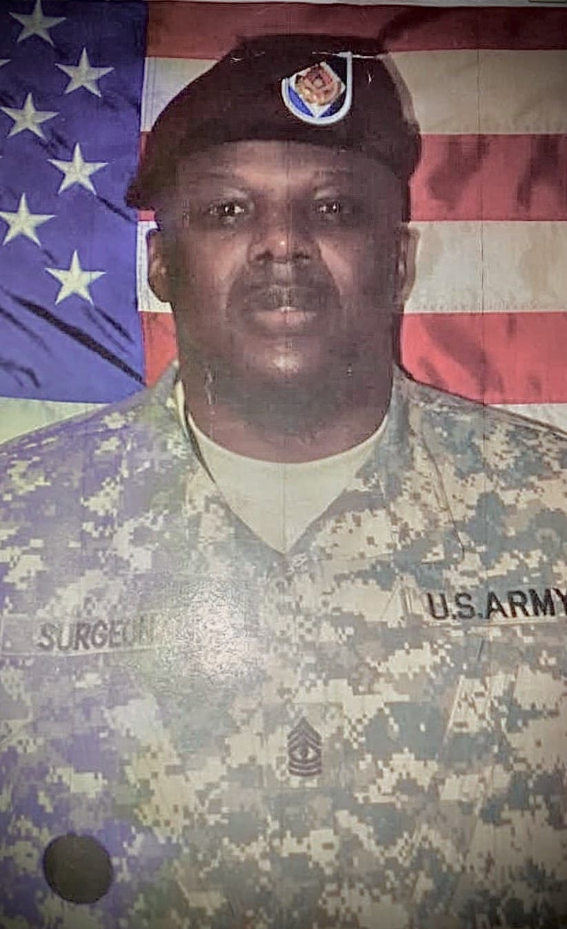 Our owner in U.S. Army uniform and beret, posed in front of an American flag